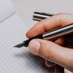 A detailed shot of a hand holding a fountain pen over graphing paper, suggesting creativity and planning.